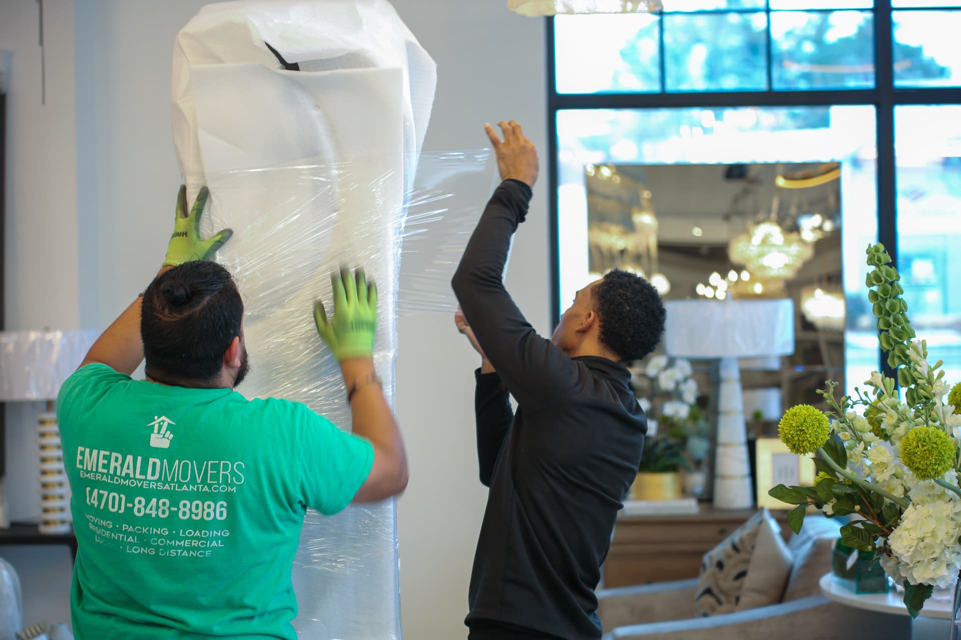 Emerald Movers wrapping a tall mirror in moving pads and stretch wrap inside a showroom