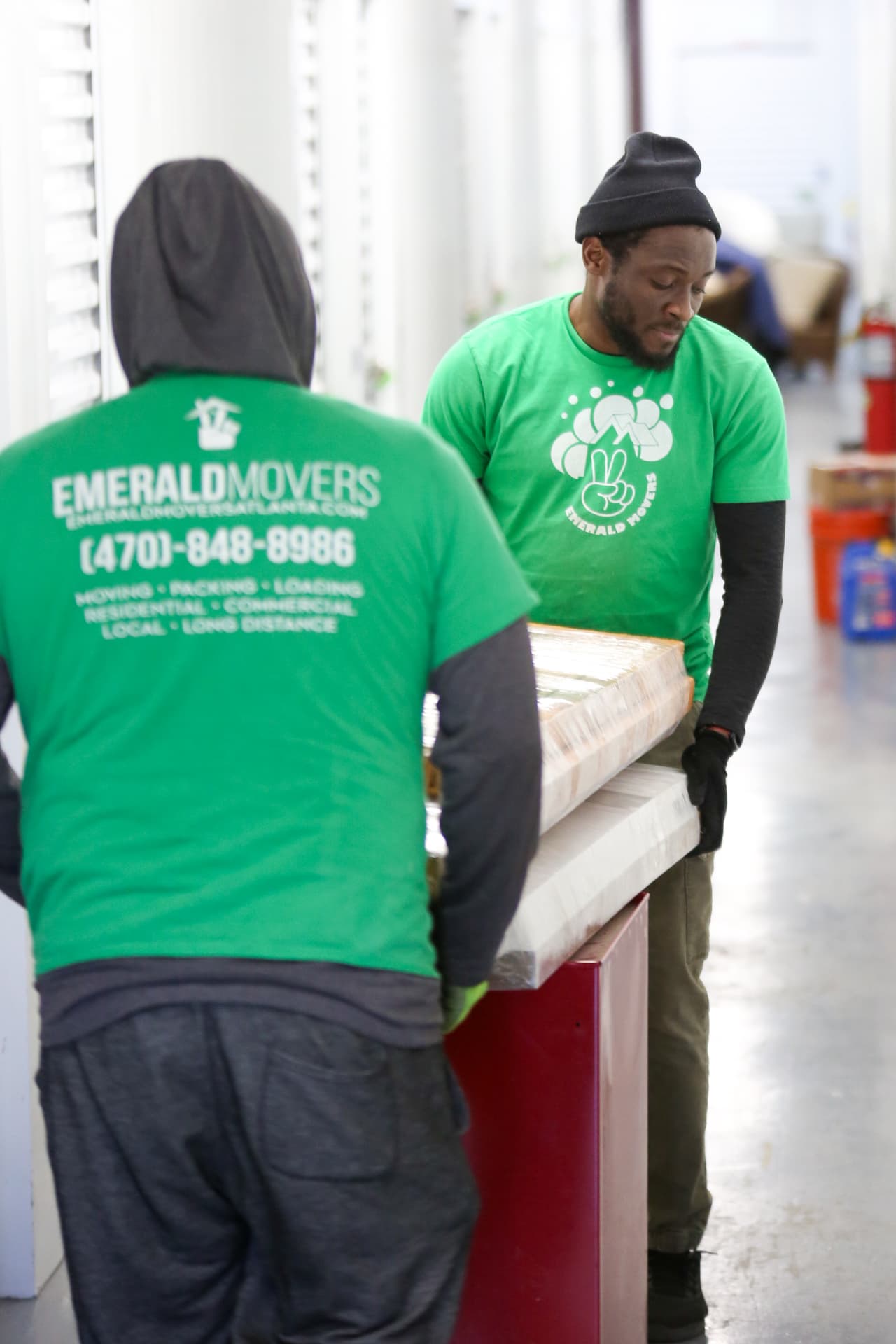 Two Emerald Movers crew members carrying a protected cabinet through a storage facility