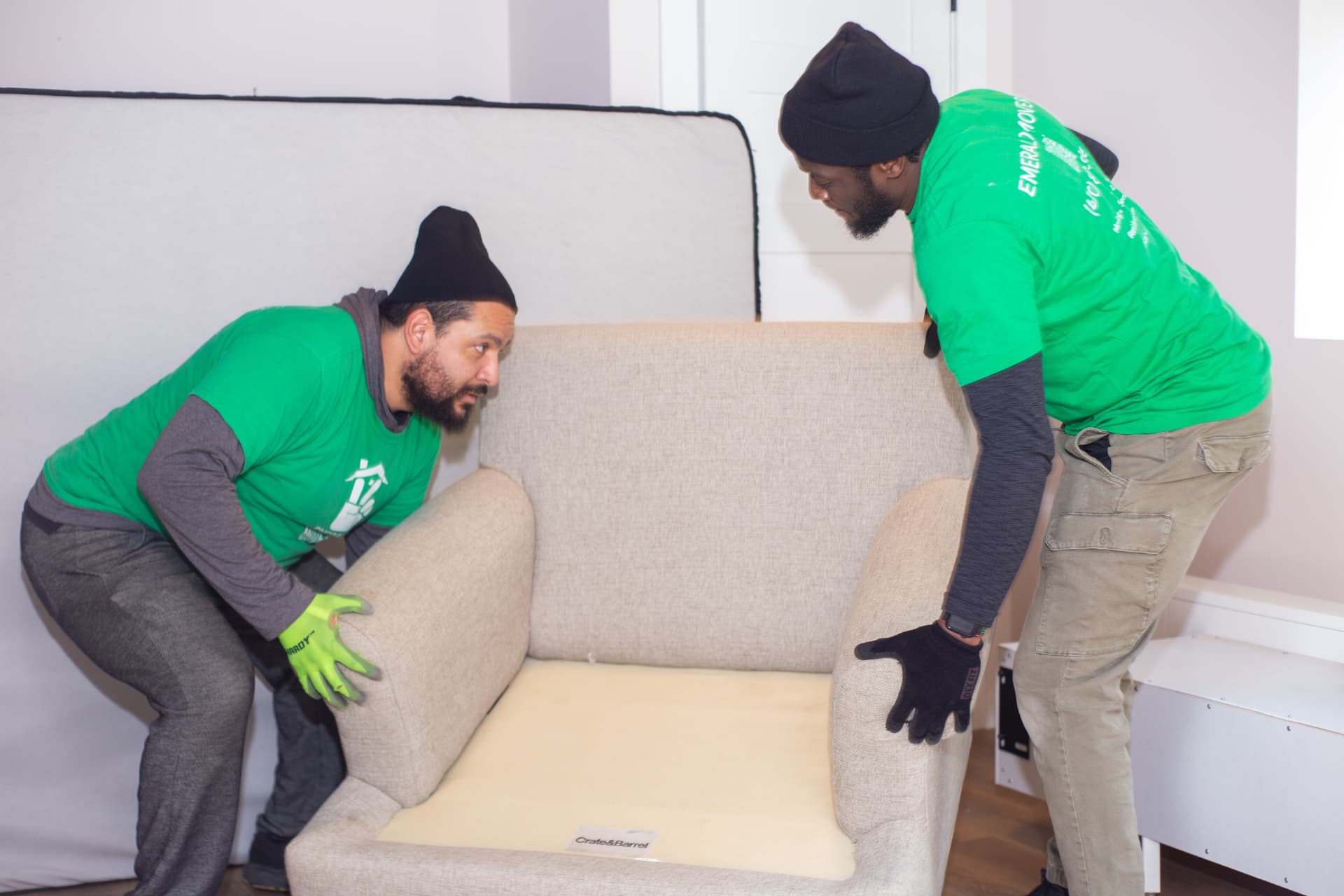 Two Emerald Movers crew members lifting an armchair together inside a home